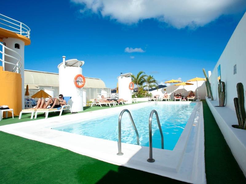 Venkovní bazén s lehátky a slunečníky pod jasně modrou oblohou.