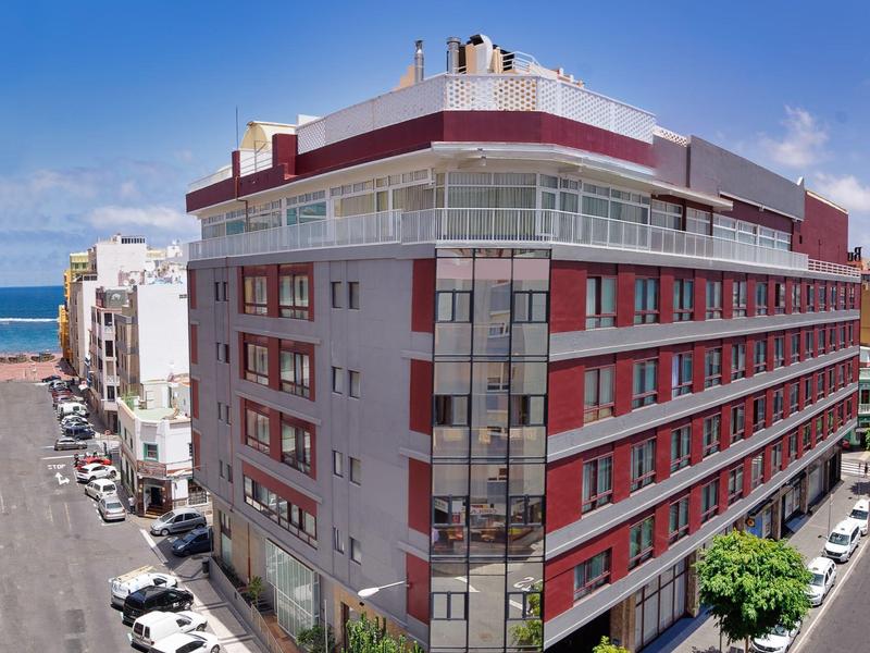 Moderní vícepatrový hotel u oceánu s zaparkovanými auty a jasnou modrou oblohou.