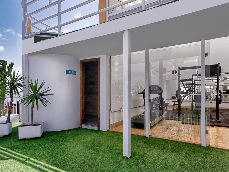 Venkovní patio s umělým trávníkem, rostlinami a posilovnou viditelnou přes skleněné dveře.