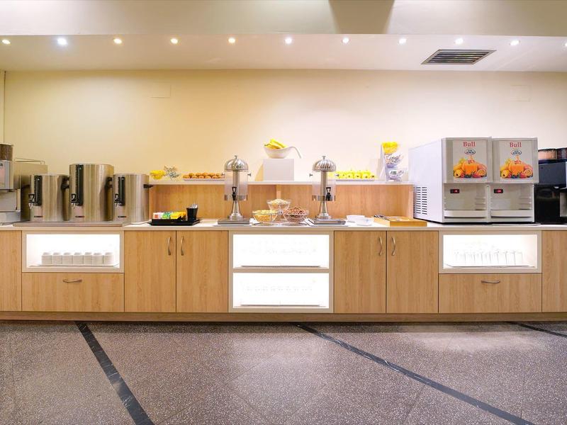 Moderní bufet se kávovary, dávkovači džusů a pečivem na dřevěném pultu.