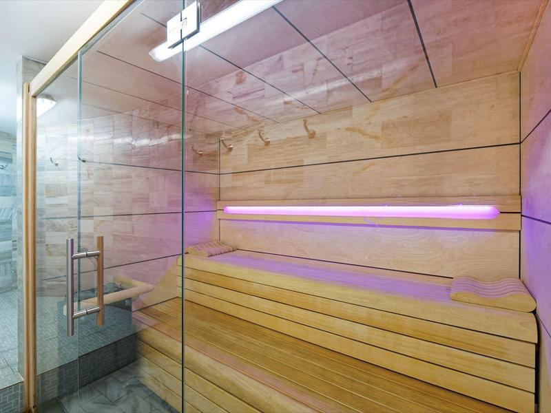 Moderní dřevěná sauna se skleněnými dveřmi a fialovým ambientním osvětlením v hotelovém spa.