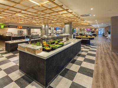 Großer moderner Buffetbereich mit Gemüse, Salaten und verschiedenen Essstationen, helle Beleuchtung.