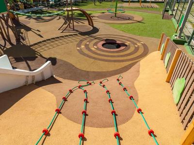 Kinderspielplatz mit Kletternetz, Wellenrutsche, Sandbereich und Palmen im Hintergrund.