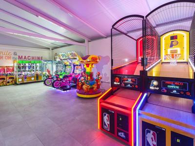 Bunte Spielhalle mit Bowling-Automaten, Kinderkarussell und Greifautomaten in hellem Raum.