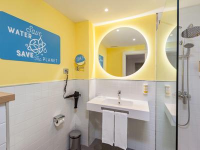 Modernes Badezimmer mit gelben Wänden, rundem Spiegel, Waschbecken, Duschkabine und Umweltschild.