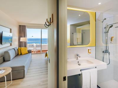Modernes Hotelzimmer mit Meerblick, Sofa, Balkon, Bad mit Dusche und großem Spiegel.