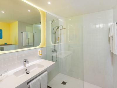 Moderner, heller Badraum mit Glasdusche, großem Spiegel und weißem Waschbecken.