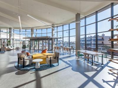 Bright, modern lounge with large windows, colorful seating, and a ping pong table.