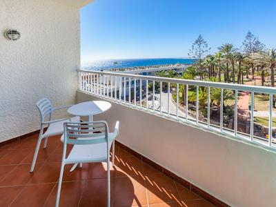 Balcony with table and two chairs overlooking the sea and a park.