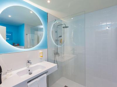 Modern bathroom with round illuminated mirror and glass shower.