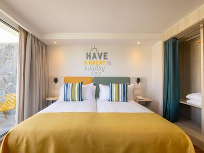 Modernes Hotelzimmer mit großem Bett, gelber Bettdecke und offener Garderobe.