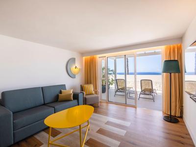 Helles Wohnzimmer mit blauem Sofa, gelbem Tisch und Terrasse mit Meerblick.