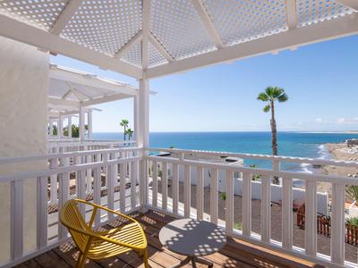 Balkon mit weißem Geländer und gelbem Stuhl mit Blick auf das Meer und Palmen