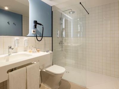 Modernes Hotelbadezimmer mit Dusche, Toilette und Waschbecken in neutralen Farben.