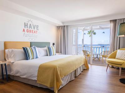 Modernes Schlafzimmer mit Doppelbett, gelben Akzenten und Balkon mit Meerblick.