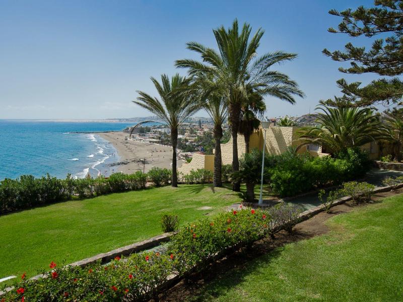 Zelená zahradní plocha s palmami s výhledem na pláž a moře.