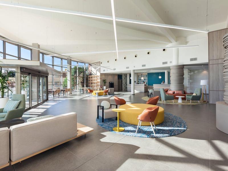 Prostorná hotelová lobby s moderním nábytkem, posezením a dostatkem přirozeného světla.