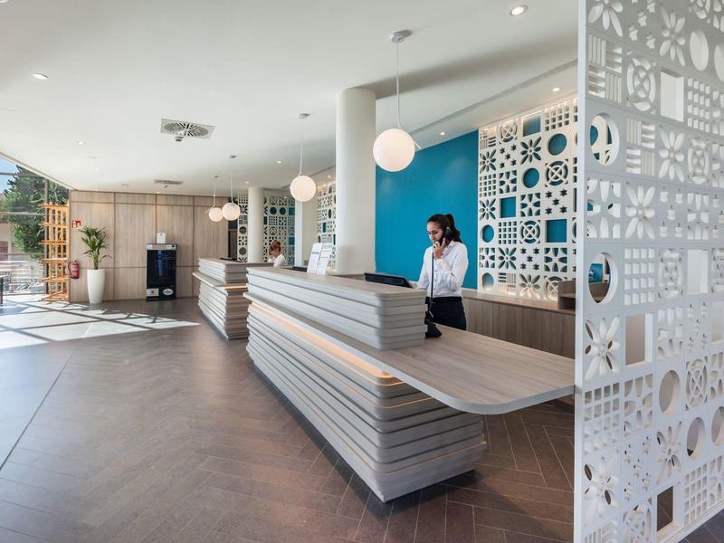 Moderní hotelová recepce s pultem, modrým pozadím a dekorativní příčkou