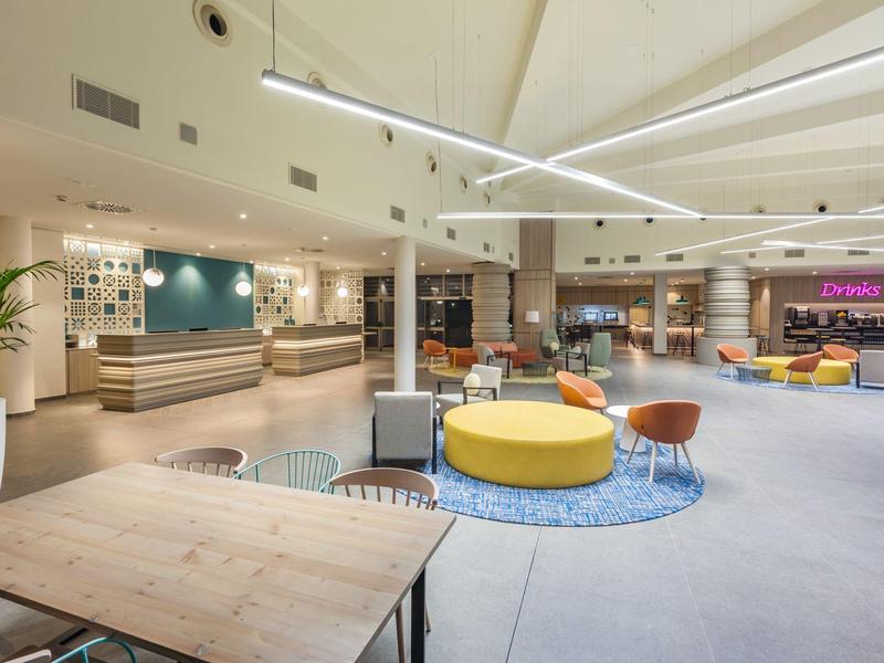 Moderní otevřená hotelová hala se sedacími skupinami, pulty a osvětlením.