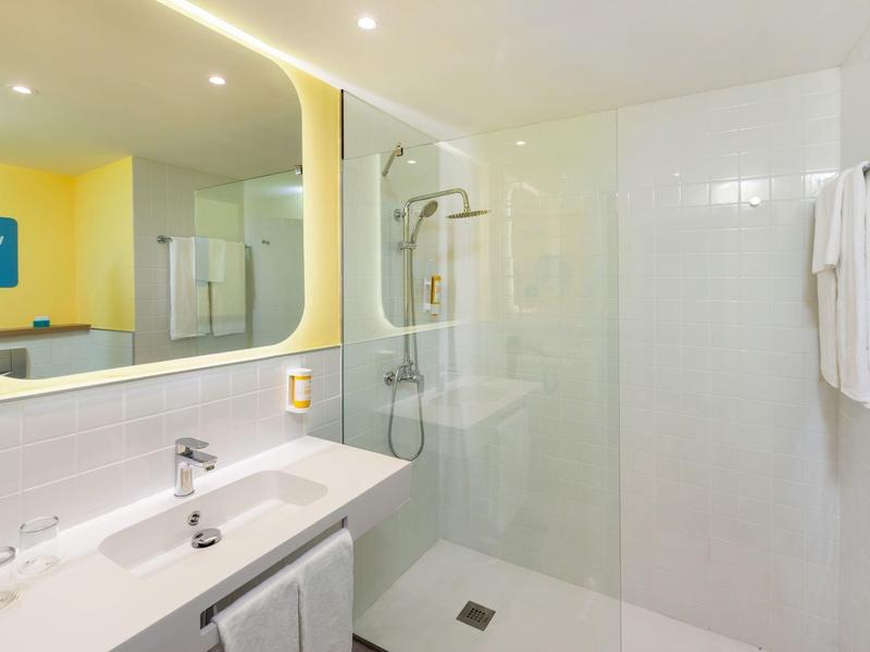 Světlá koupelna s osvětleným zrcadlem, skleněnou sprchou a bílými ručníky.