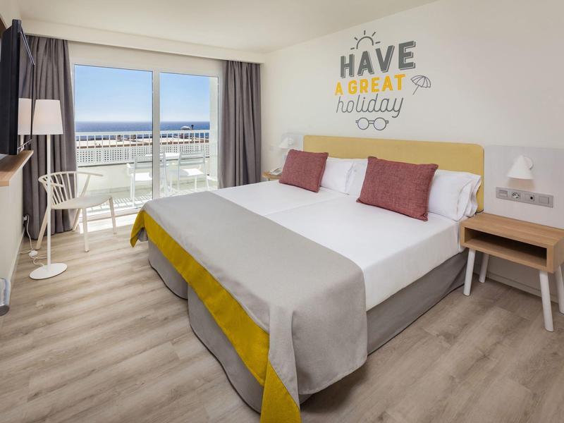 Moderní hotelový pokoj s manželskou postelí, balkonem a výhledem na moře.