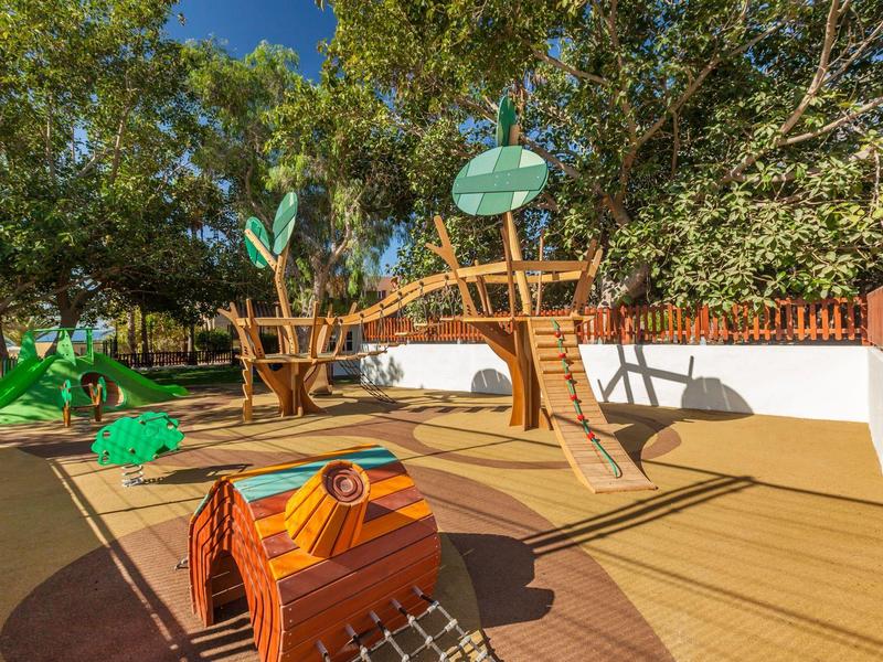 Dětské hřiště s prolézačkou a dřevěnými hračkami na slunném venkovním prostoru.