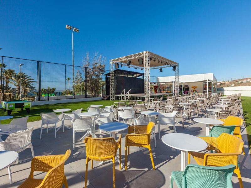 Moderní venkovní prostor s barevnými židlemi a stoly pod jasnou modrou oblohou