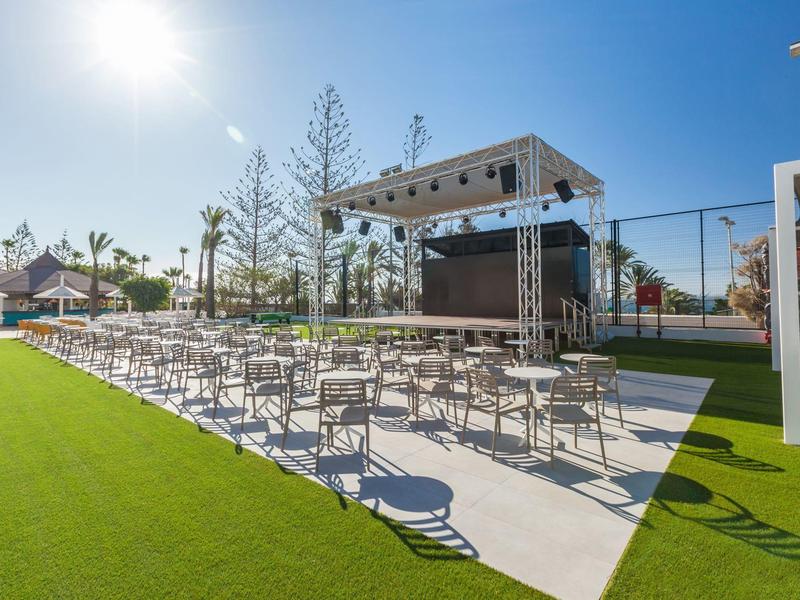 Venkovní prostor pro akce s řadami židlí a pódiem pod jasnou oblohou na zelené trávě