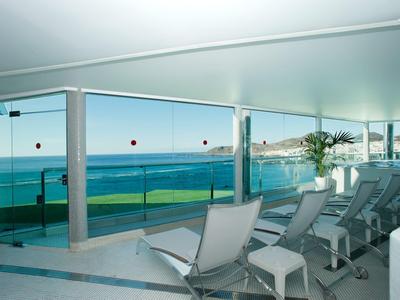 Balkon met ligstoelen met uitzicht op de oceaan en kustlijn onder een heldere lucht.