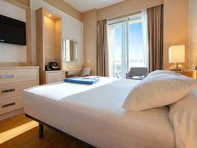 Licht ingericht hotelkamer met groot bed, tv en balkon met zeezicht.