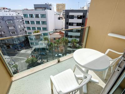 Balkon met witte stoelen en tafel, uitzicht op stadsgebouwen bij heldere lucht.