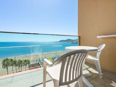 Twee witte stoelen op balkon met glazen balustrade en zeezicht onder blauwe lucht