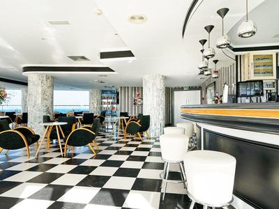 Area bar moderna di un hotel con pavimento a scacchi bianco e nero e sedute eleganti.