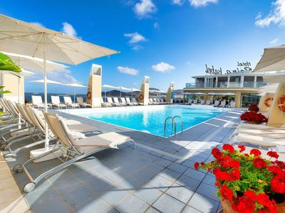 Area piscina moderna con lettini e ombrelloni, cielo azzurro e vista mare.