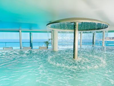 Piscina moderna dell'hotel con fontana a cascata e vista sull'oceano attraverso finestre di vetro.