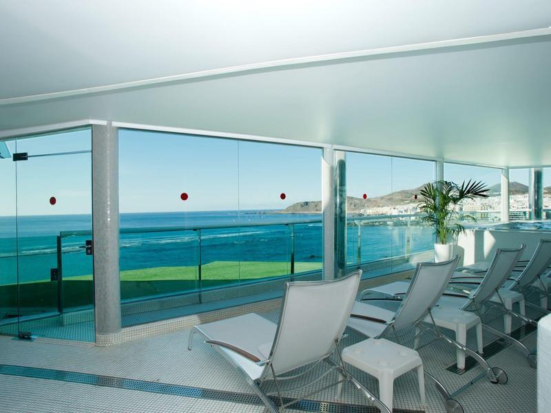 Balkon met ligstoelen met uitzicht op de oceaan en kustlijn onder een heldere lucht.