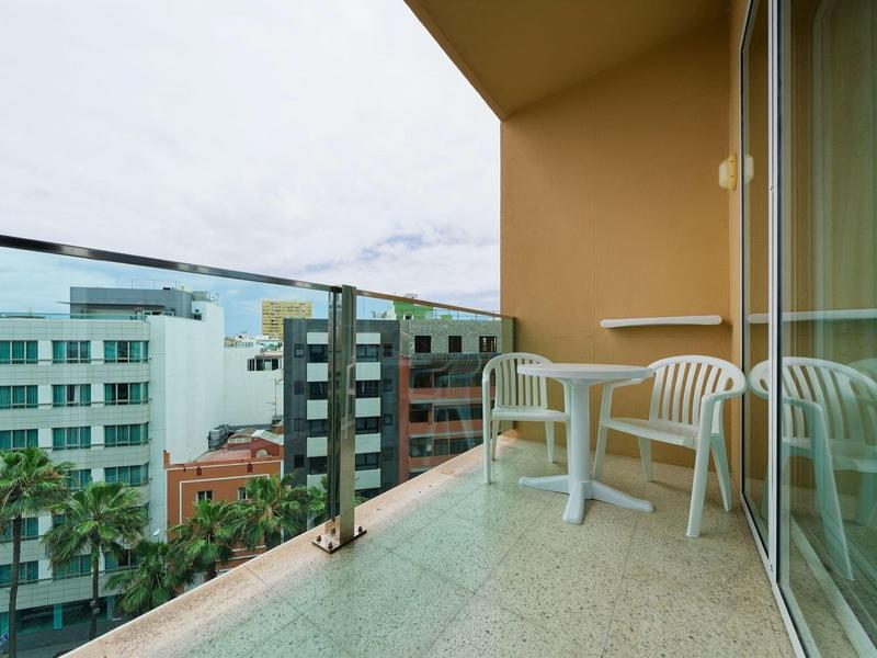 Balkon met twee witte plastic stoelen en een tafel met glazen balustrade en stadszicht.