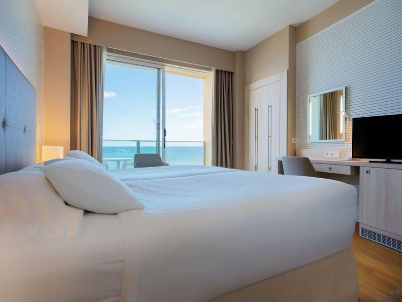 Lichte hotelkamer met tweepersoonsbed, zeezicht en moderne inrichting.