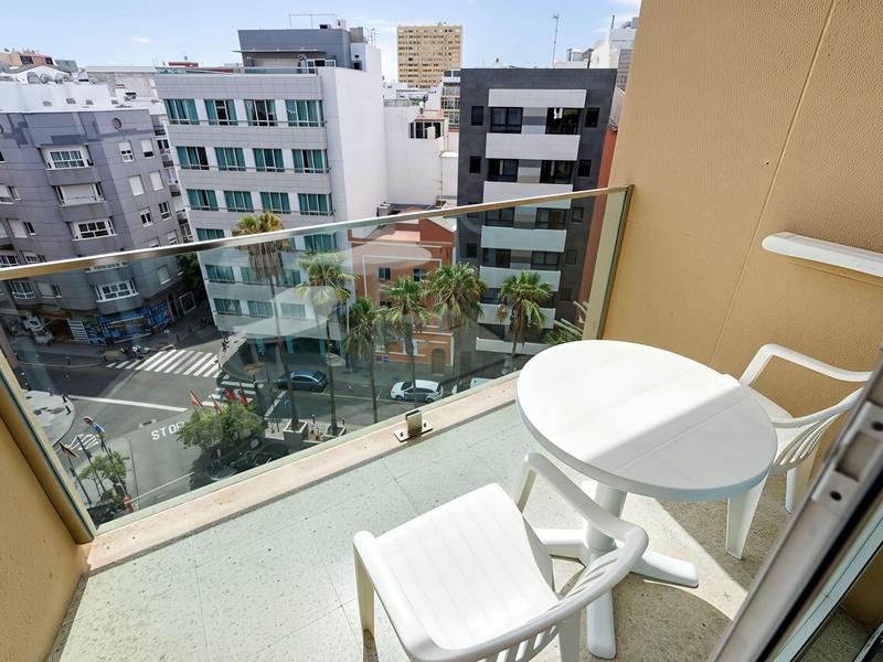 Balkon met witte stoelen en tafel, uitzicht op stadsgebouwen bij heldere lucht.