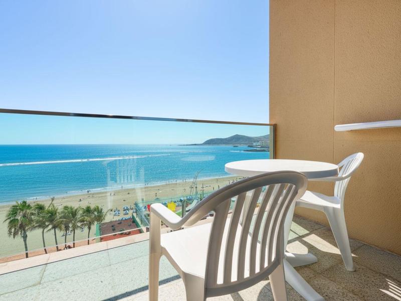 Twee witte stoelen op balkon met glazen balustrade en zeezicht onder blauwe lucht