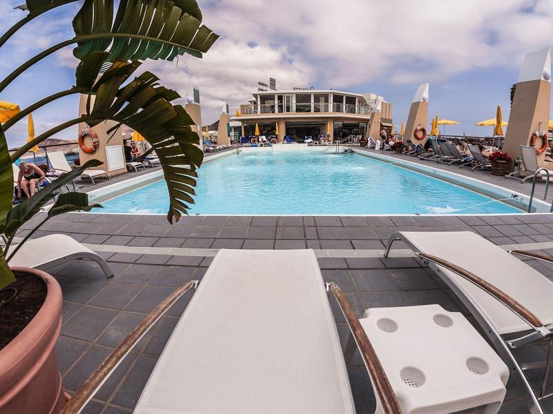 Zwembad met ligstoelen, parasols en een heldere lucht boven een modern hotel.