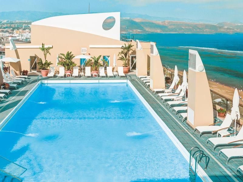 Dakterraszwembad met ligstoelen en uitzicht op de oceaan bij een hotel aan de kust.