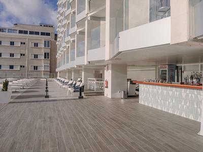 Espace extérieur moderne d'hôtel avec bar et terrasse en bois sous ciel clair.