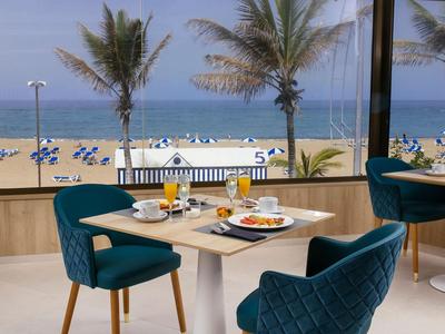 Helles Restaurant mit Blick auf Strand, Palmen und blauen Stühlen am Meer.