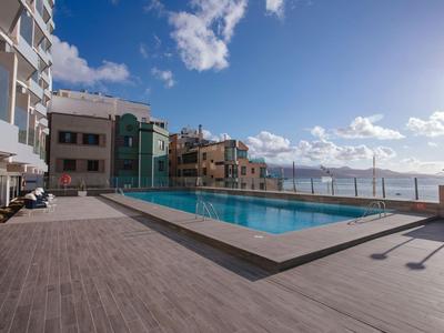 Moderner rechteckiger Pool auf einer Terrasse mit Meerblick und klarem Himmel.