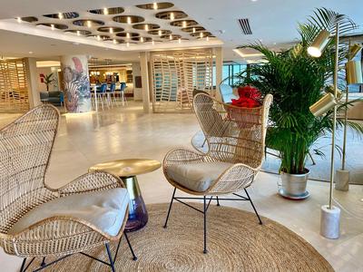 Stylische Sitzgruppe mit Geflechtsesseln und Pflanzen in einem modernen Hotelinterieur.