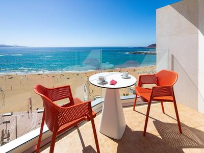 Balkon mit zwei roten Stühlen und kleinem Tisch mit Meerblick am Strand.