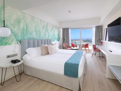 Modernes Hotelzimmer mit Doppelbett, TV, Balkon und Meerblick in hellem Farbton.