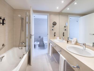 Helles Badezimmer mit Badewanne, Doppelwaschbecken und Blick ins WC.