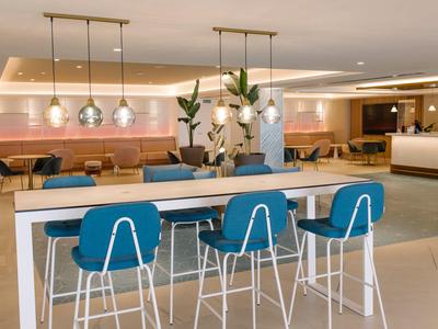 Salon d'hôtel moderne avec tabourets bleus, tables longues et ambiance détendue.